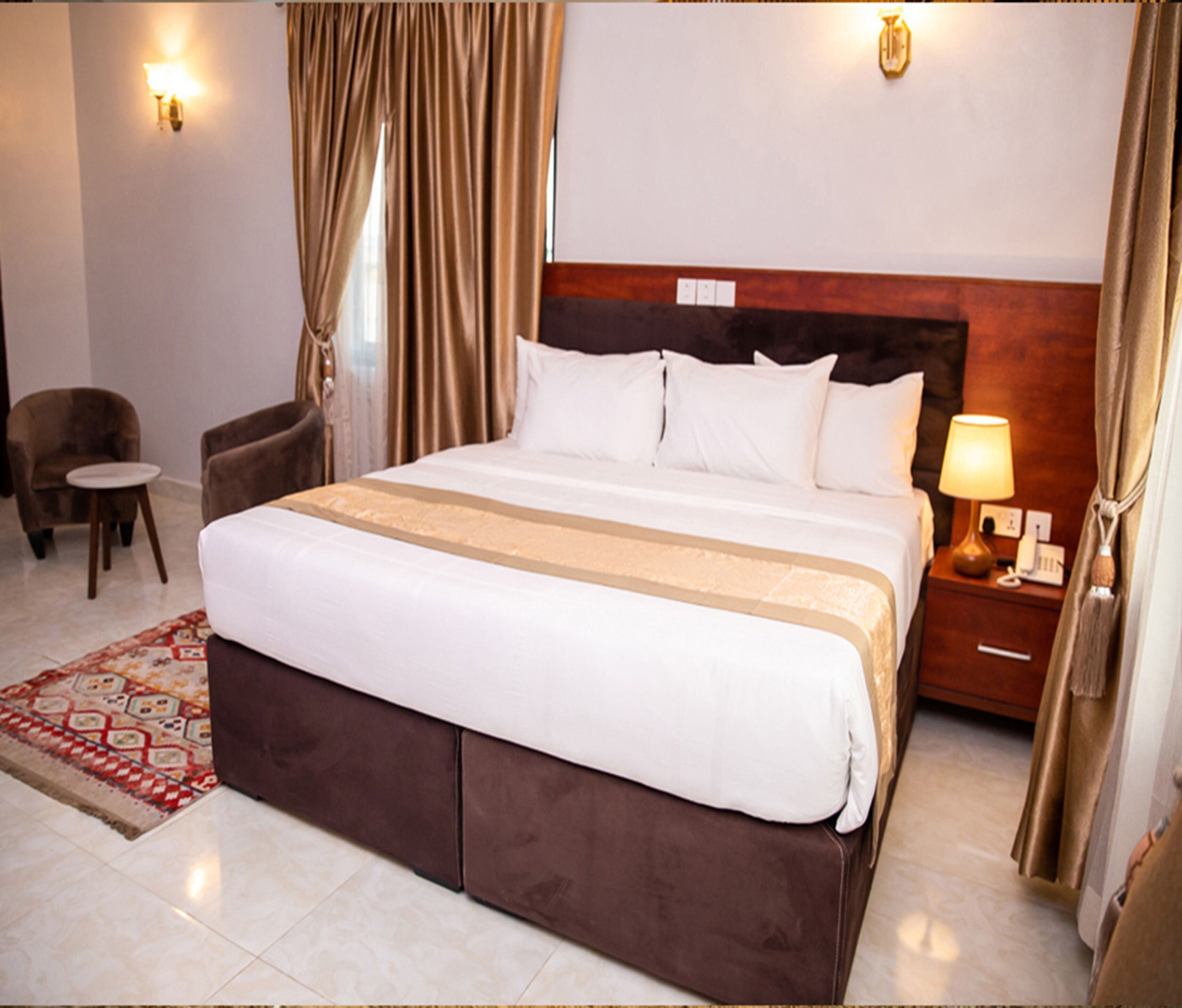 A hotel room with a large bed, a nightstand with a lamp, a chair, and a small table.