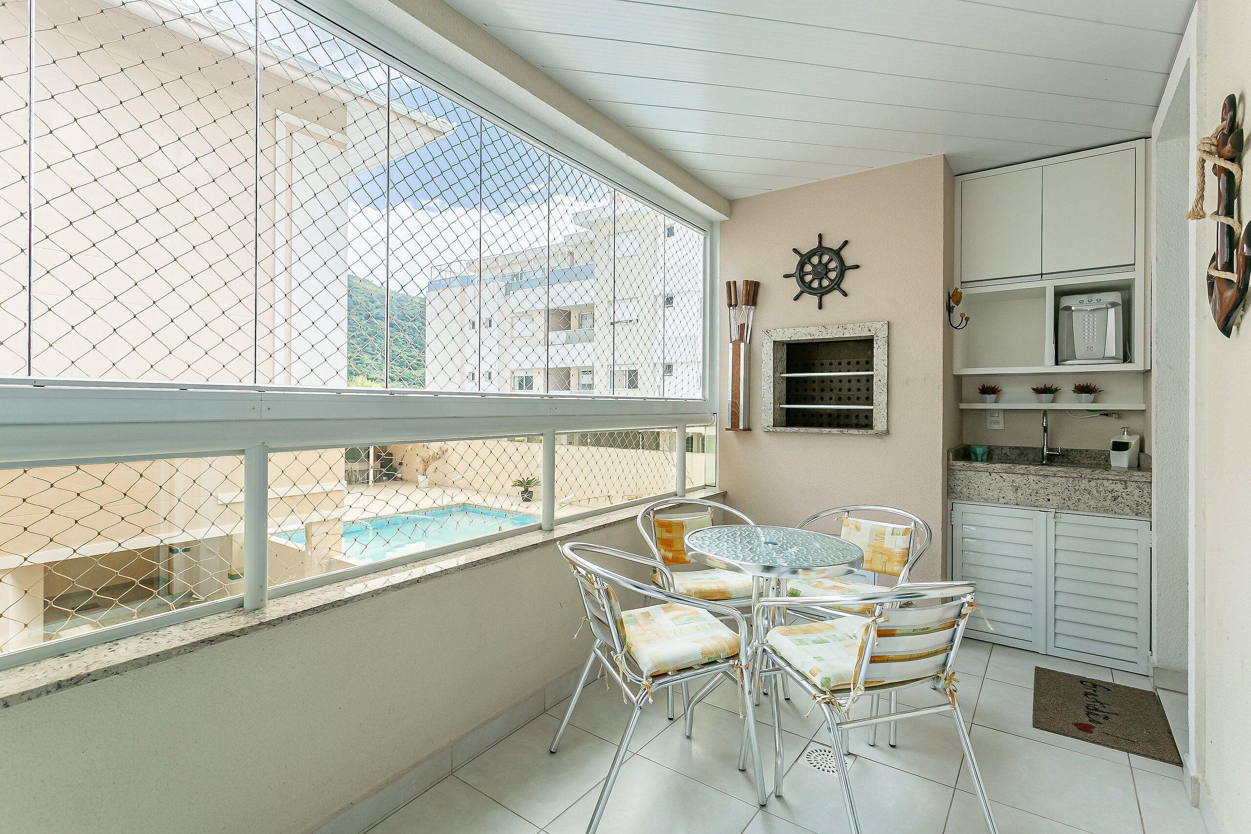 A balcony with a table and chairs, a view of a swimming pool, and a kitchen area with cabinets and a microwave.