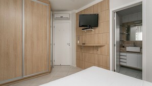Een slaapkamer met een bed, kledingkast, televisie, en een badkamer met een wastafel en spiegel.