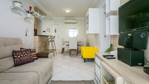 Een moderne woonkamer met een bank, een televisie en een eethoek met een gele stoel.