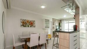 Een moderne keuken met een centraal eiland, witte kasten en een eetgedeelte met een glazen tafel en stoelen.