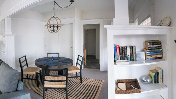 A living room with a gray sofa, a round table with chairs, a bookshelf with books, and a patterned rug. - STAY 5 MINUTES  AWAY (Oakland)