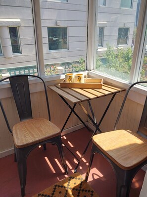 Ein kleines Zimmer mit Fenster, zwei Holzstühle, ein Tisch mit Tablett und einem gemusterten Teppich.