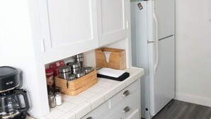 A kitchen with white cabinets, a white refrigerator, a wooden table, and a coffee maker. - STAY 5 MINUTES  AWAY (Oakland)