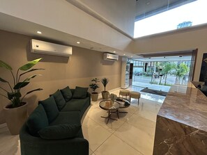 Un moderno hall con un sofá, una mesa de centro, plantas en macetas y vistas al exterior.