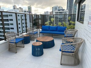 Una terraza en la azotea con mobiliario de mimbre, un sofá azul y vistas a la ciudad.