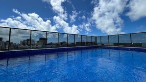 Ein Pool auf dem Dach mit Blick auf die Stadt, bewölkter Himmel und einer Glasbrüstung.