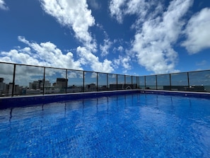 Una piscina en la azotea con vistas a la ciudad, cielo despejado y barandilla de vidrio.