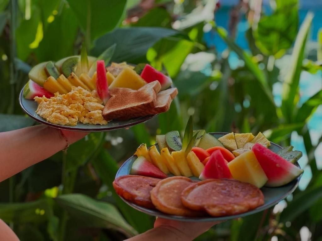 Two plates of food with fruits and scrambled eggs, held by a person.
