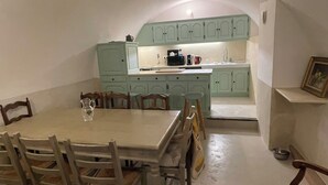 Et spiseområde med et bord og stole, et køkken med lysegrønne skabe, og et lille spisebord i baggrunden.