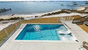 A rectangular pool with a wooden deck and a view of the beach and water.