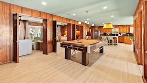 A spacious room with a pool table, wooden paneling, and a kitchen area. - Tide & Timber (Gulf Shores)