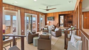 A spacious living area with a wooden interior, a ceiling fan, and a view to a balcony.