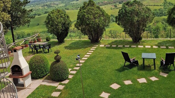 A landscaped garden with a patio area, outdoor seating, and a view of rolling hills.