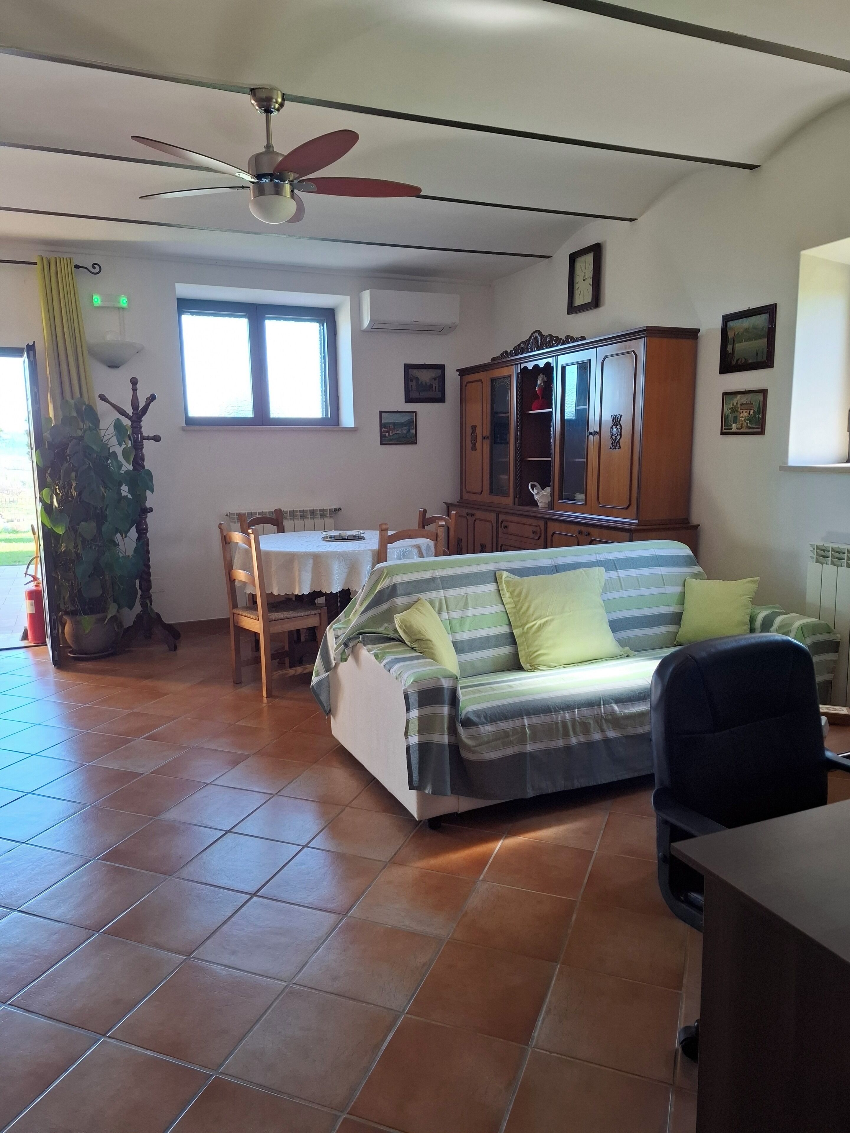 Ein Wohnzimmer mit einer Couch, einem Esstisch, Stühlen, einem Deckenventilator und einem Schrank.