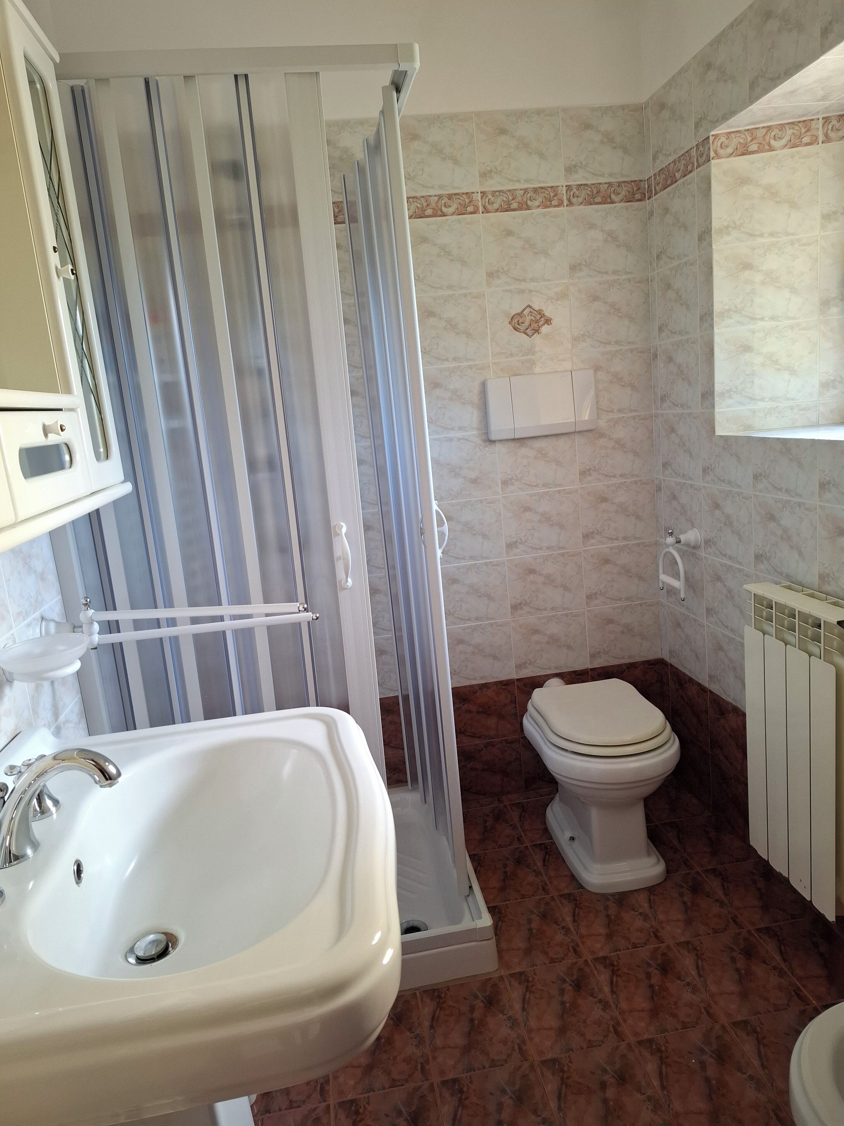 Un bagno con cabina doccia, lavandino, water e termosifone.