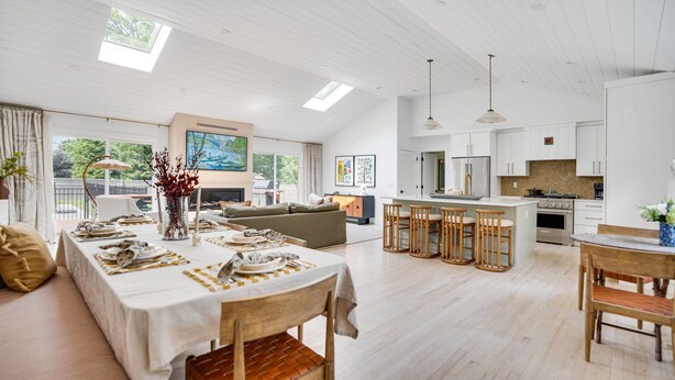Un amplio salón con una mesa de comedor lista para seis personas, un sofá y una cocina con armarios blancos y una isla grande.
