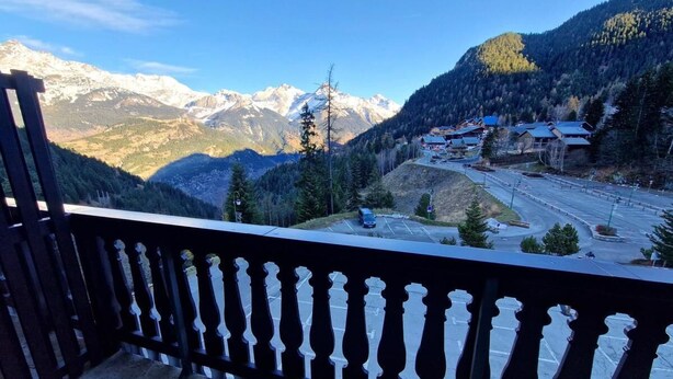 En balkon med udsigt til et bjerglandskab og en parkeringsplads.