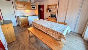 Et kompakt køkken med træskabe, en mikrobølgeovn og en brødrister. Der er et spisebord med et mønstret borddække og bænke.