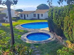 A residential swimming pool with a stone border, surrounded by a well-maintained lawn and a hedge.