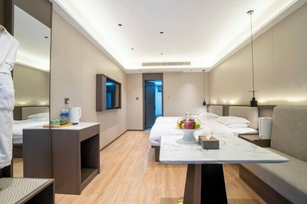 A modern hotel room with a bed, bedside table, and a small table with fruit.