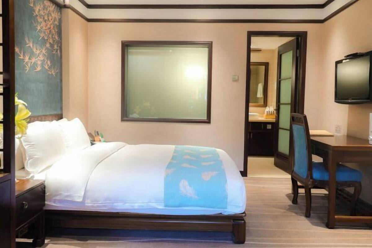 A hotel room with a bed, a desk, a chair, a television, and a bathroom visible through an open door.