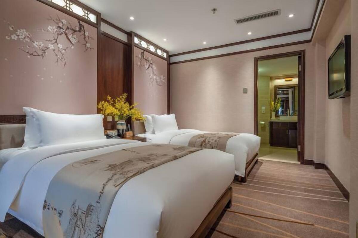 A hotel room with two beds, a television, a mirror, and a door leading to a bathroom.