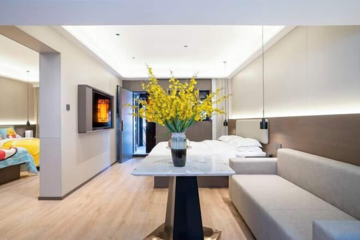 A modern hotel room with a bed, a sofa, a small table with a vase of flowers, and a television on the wall.