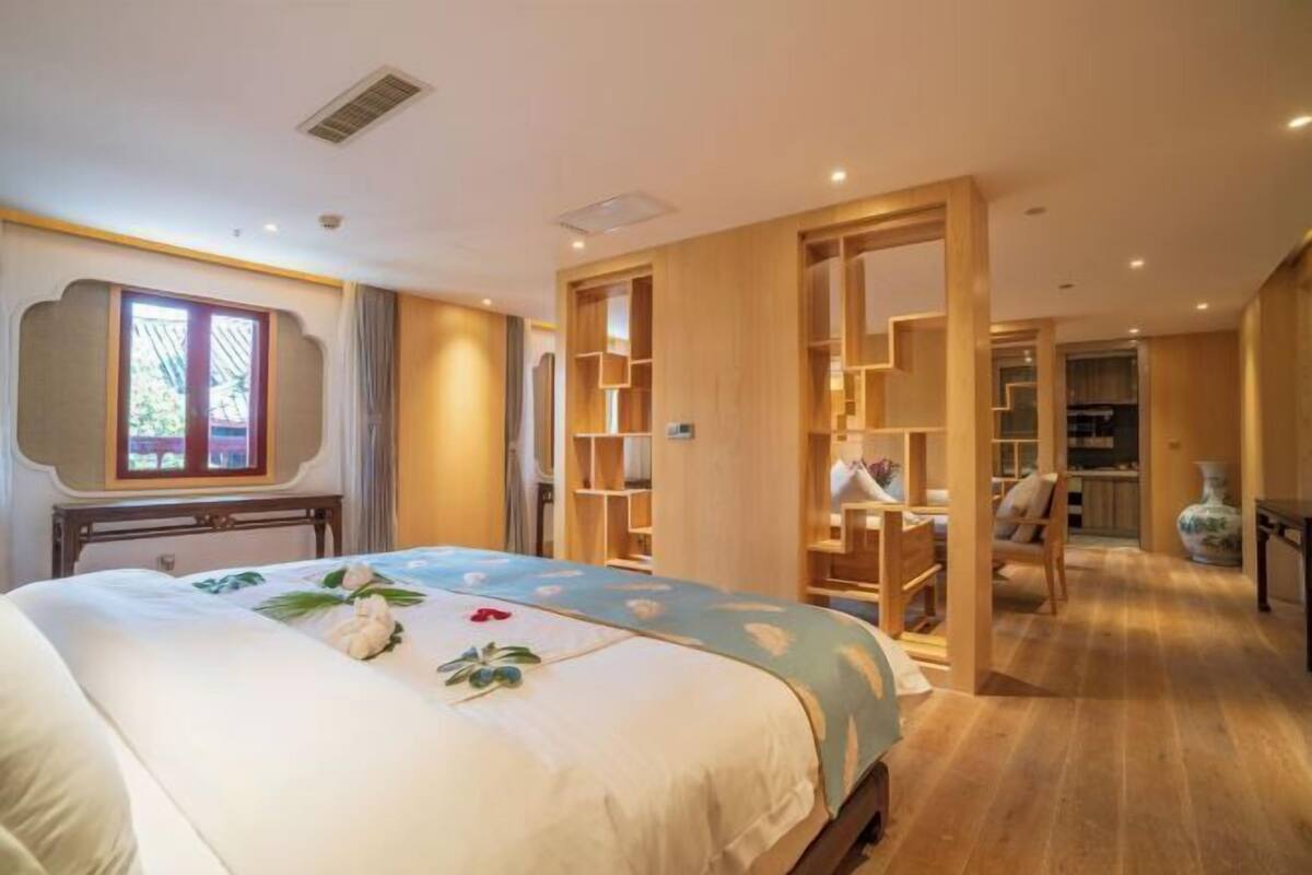 A hotel room with a bed, a wooden wardrobe, a desk, and a chair.