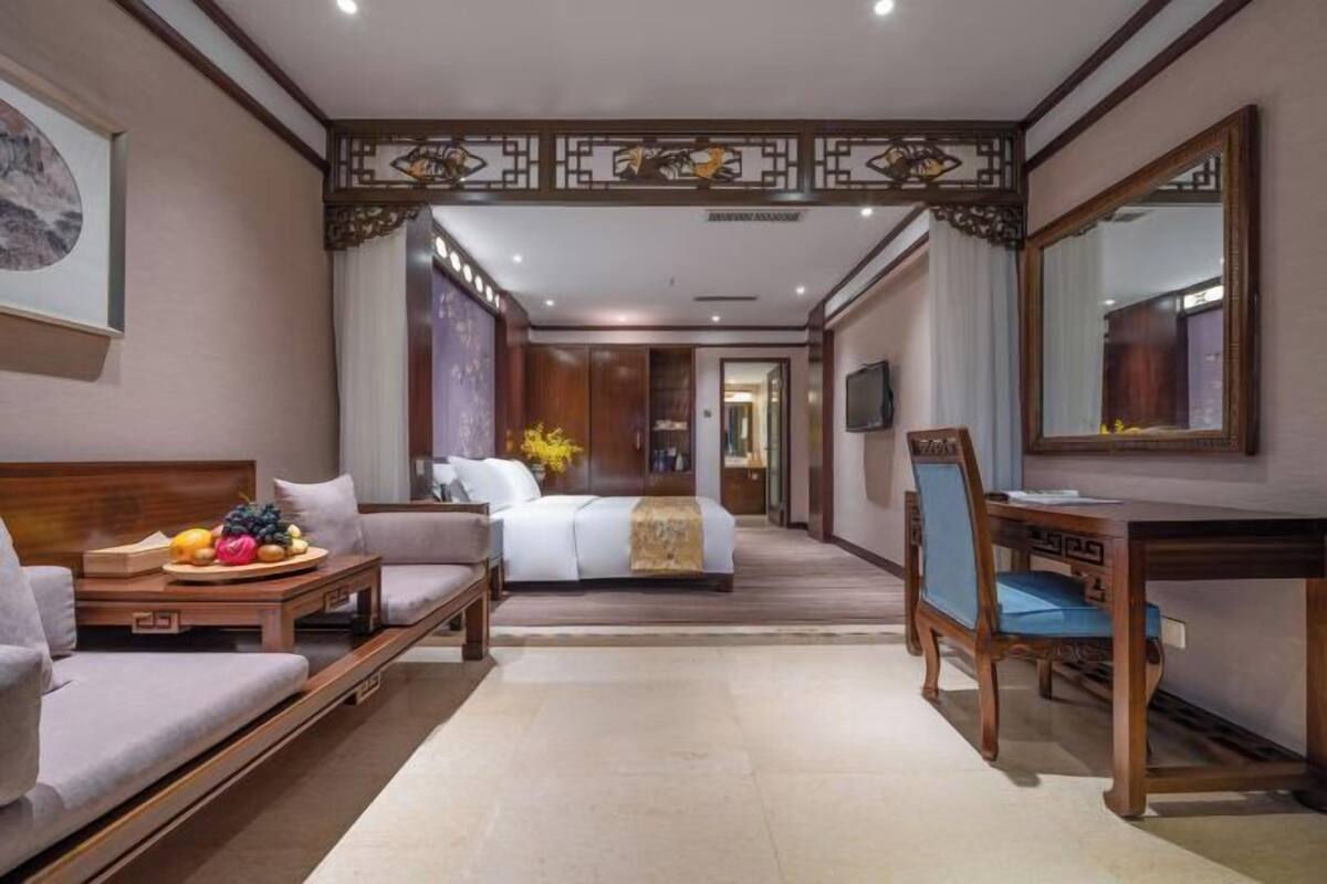 A hotel room with a bed, a sofa, a dining table, and a TV.