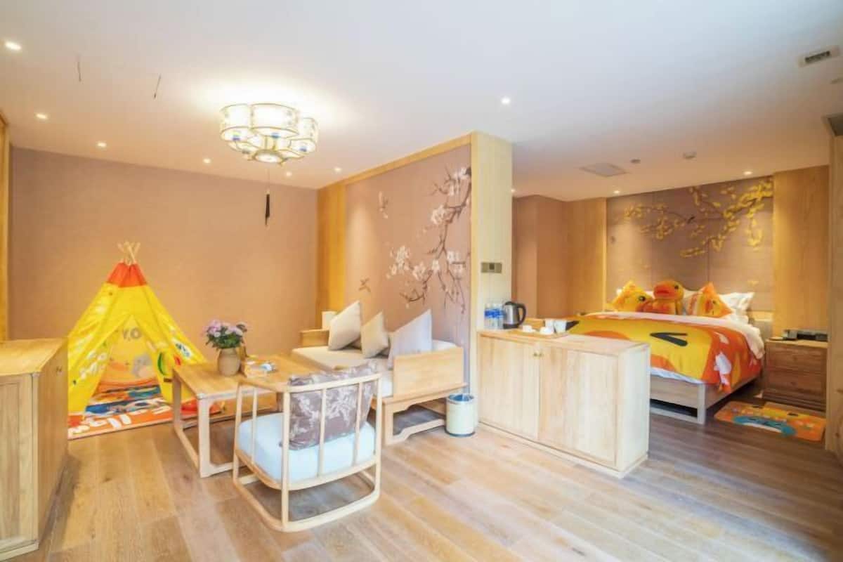 A hotel room with a bed, a desk, a chair, a small table, a tent, and a wall with a floral mural.