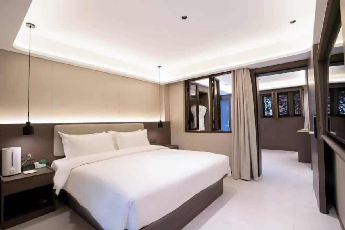 A modern hotel room with a large bed, bedside tables, a nightstand, a mirror, and a view of the outside.