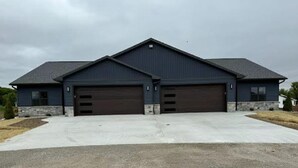 Il s’agit d’un bâtiment à deux étages, à l’extérieur bleu foncé et au toit gris. Il est doté de deux portes de garage et d’une grande allée.
