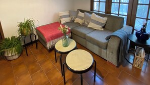Un salon avec un canapé, deux petites tables, une plante en pot et une fenêtre donnant sur des arbres.