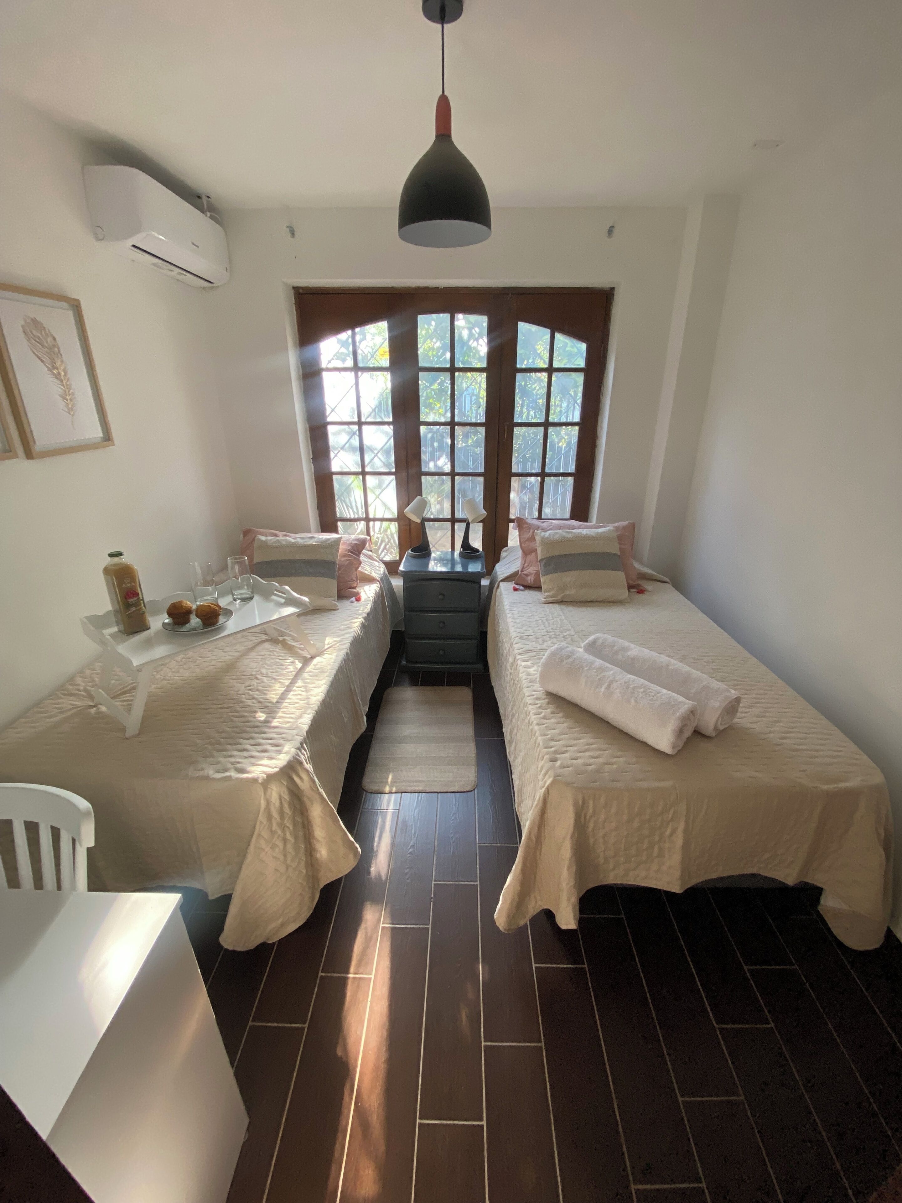 A bedroom with two beds, a desk, and a window with a view of greenery.
