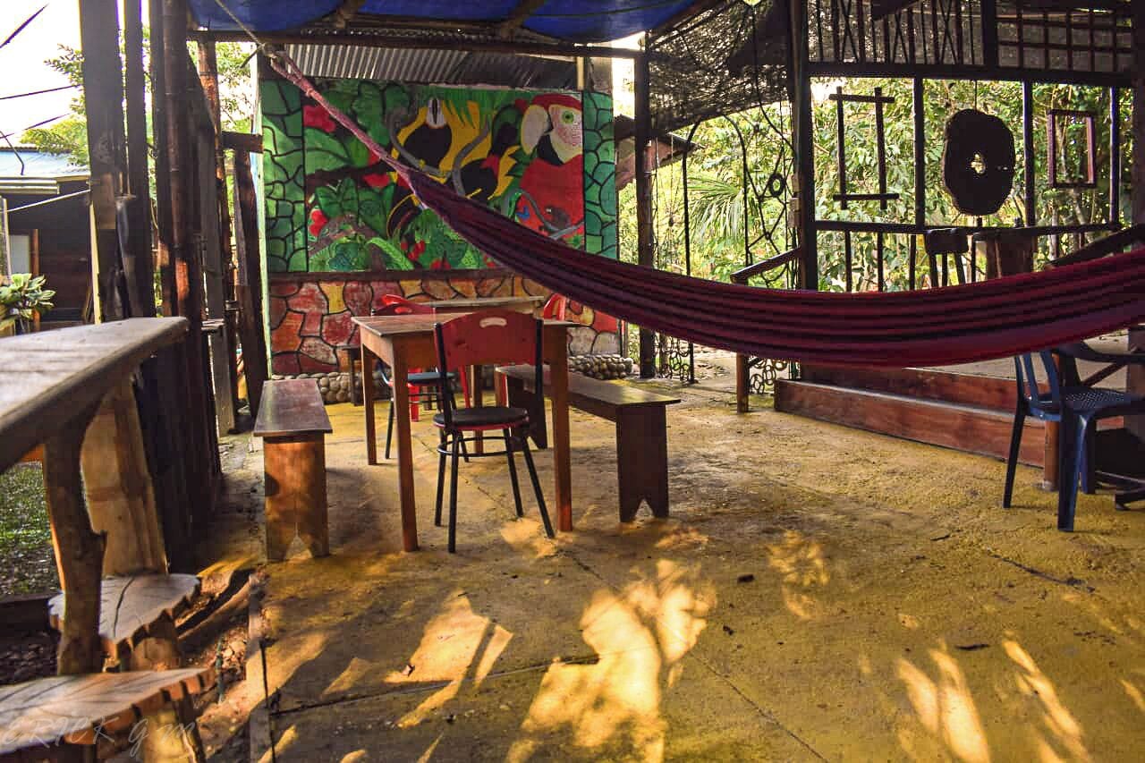 Patio esterno con amaca, tavolo, sedie e un murale sulla parete.