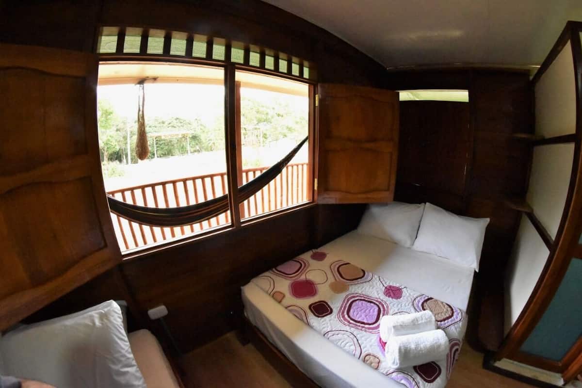 Una habitación pequeña y acogedora con una cama, una ventana con vistas a la vegetación y una hamaca afuera.