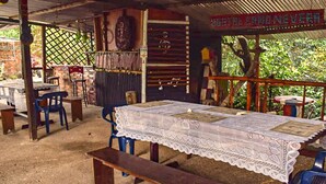 A rustic outdoor dining area with a table covered in a lace tablecloth, surrounded by blue plastic chairs and wooden benches. - Hostal Caño Nevera (La Macarena)