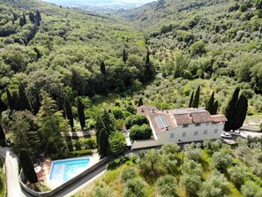 Eine Villa mit Schwimmbad, umgeben von üppiger Vegetation und Hügeln.