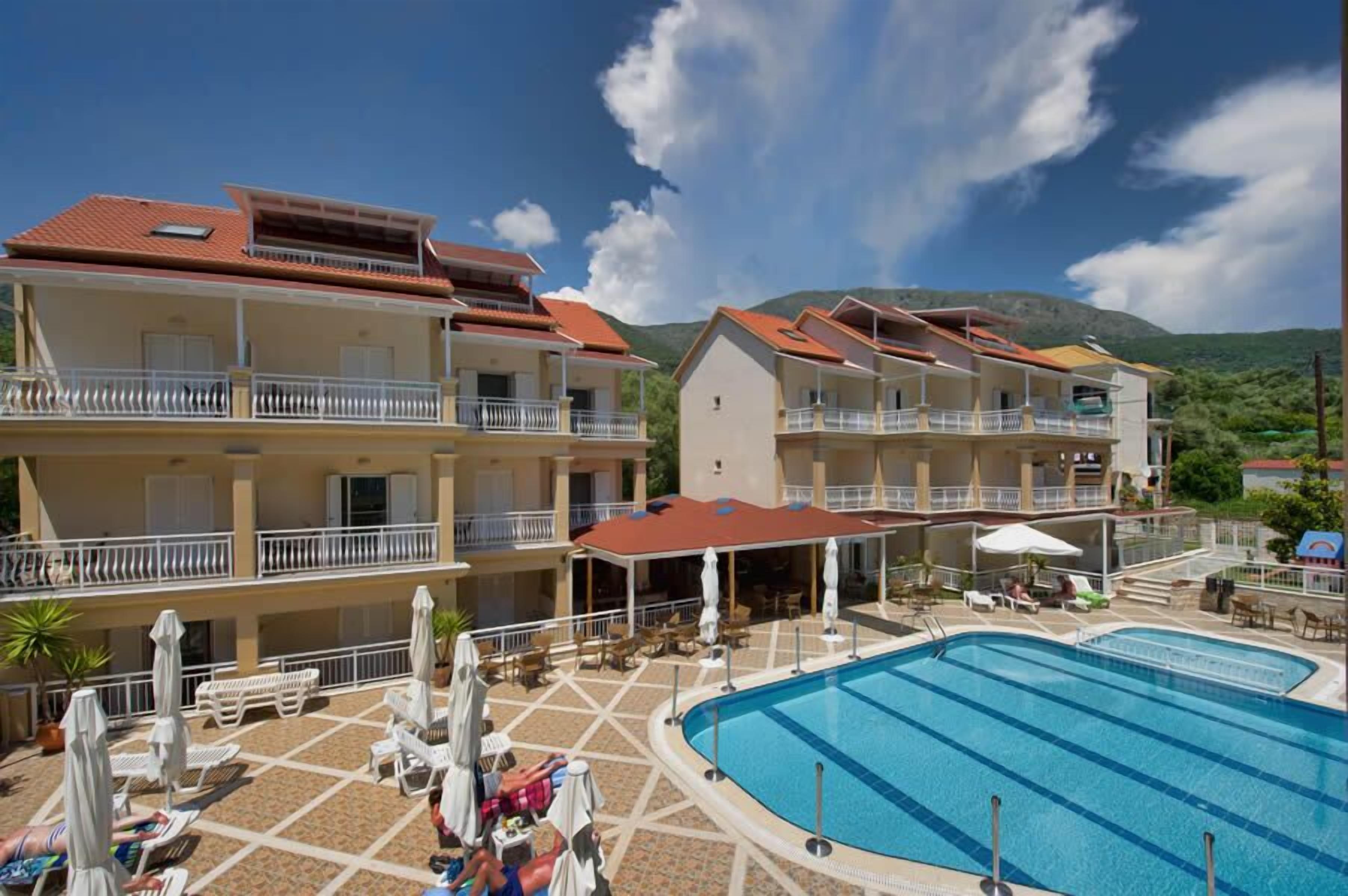 A hotel with multiple balconies, a swimming pool, and outdoor seating areas.