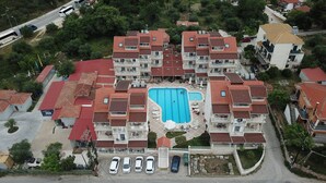 An aerial view of a residential complex with multiple buildings, a central swimming pool, and a parking area. - Elena Hotel Apartments (Parga)
