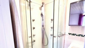 A glass-enclosed shower stall with a handheld showerhead, a small drain, and a white sink with a mirror above it.