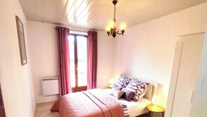 A bedroom with a bed, a bedside table, a lamp, a radiator, and a window with curtains.
