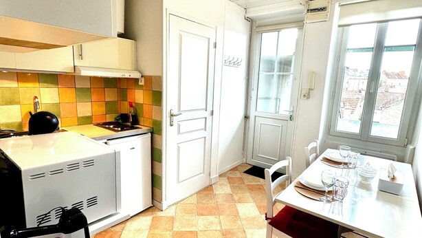 A compact kitchen with white cabinets, a tiled backsplash, and a dining area with a table set for two.