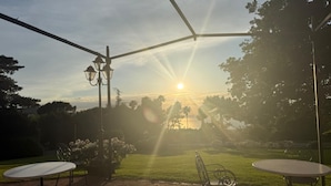 Une terrasse avec deux tables rondes et des chaises, un sol en briques et une vue sur le coucher de soleil au-dessus d’une étendue d’eau.