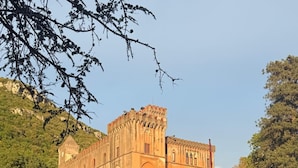 Un bâtiment historique doté d’une tour centrale et de fenêtres en arc de cercle, entouré d’une pelouse bien entretenue et d’arbres.