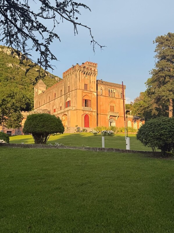 A historic building with a central tower and arched windows, surrounded by a well-maintained lawn and trees. - Luxury Designer Apartment in Parco del Principe – 15 Minutes from Positano (Piano di Sorrento)