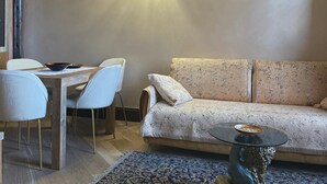 Un salon chaleureux avec une table à manger en bois, des chaises blanches, un canapé à motifs et un luminaire mural original.