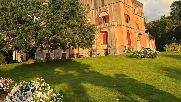 Un bâtiment historique doté d’une tour, entouré de pelouses bien entretenues et de plantes en fleurs.