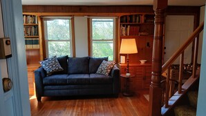 Una sala de estar acogedora con un sofá azul oscuro, estanterías de madera, suelo de madera y una escalera.